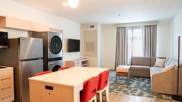 Een compacte hotelkamer met kitchenette, een zithoek met rode stoelen, een bank en een groot raam met gordijnen.