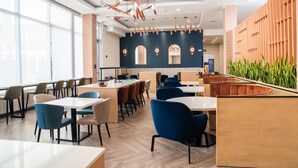 A modern restaurant interior with high ceilings, pendant lighting, and a mix of seating arrangements including tables and booths. - Homewood Suites By Hilton Corpus Christi Downtown (Corpus Christi)