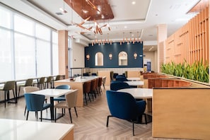 A modern restaurant interior with high ceilings, pendant lighting, and a mix of seating arrangements including tables and booths. - Homewood Suites By Hilton Corpus Christi Downtown (Corpus Christi)