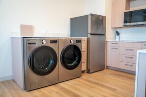 A compact kitchen with a washing machine, a refrigerator, and wooden cabinets. - Homewood Suites By Hilton Corpus Christi Downtown (Corpus Christi)