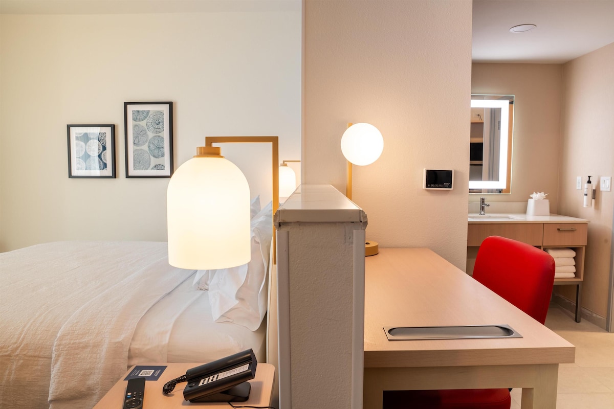 A hotel room with a bed, a desk with a lamp, a phone, and a mirror.