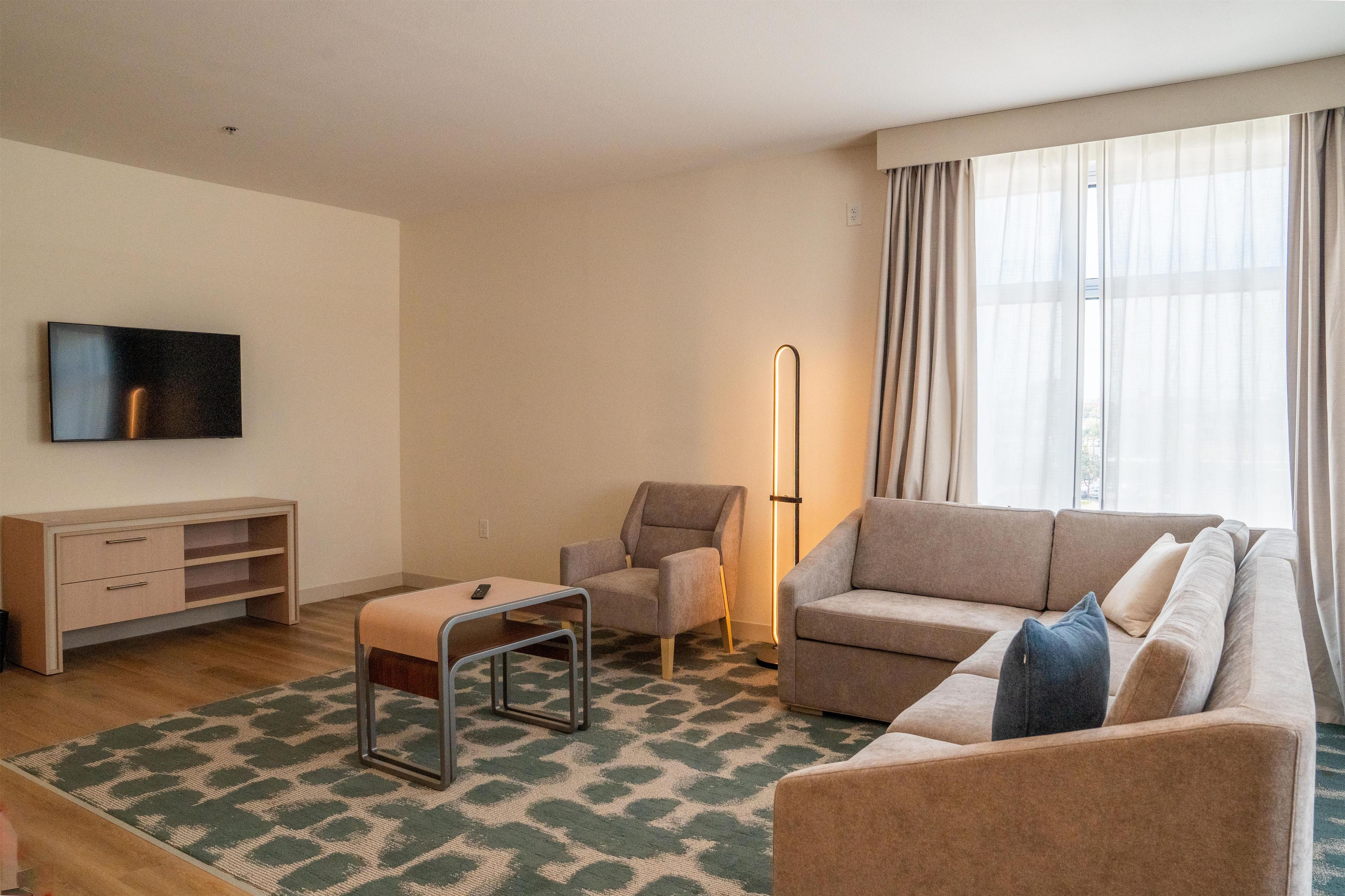Una sala de estar moderna con sofá, sillón y televisor en la pared.