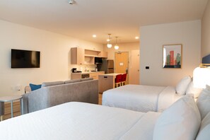 Una habitació d'hotel amb dos llits, una cuineta, zona de menjador i un televisor.