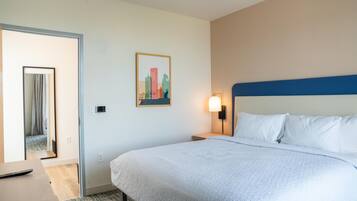 Une chambre d’hôtel avec un lit, une table de chevet, une lampe fixée au mur, un tableau et une porte donnant sur une autre pièce.