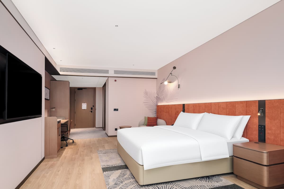 A modern hotel room with a large bed, bedside table, and a flat-screen TV.