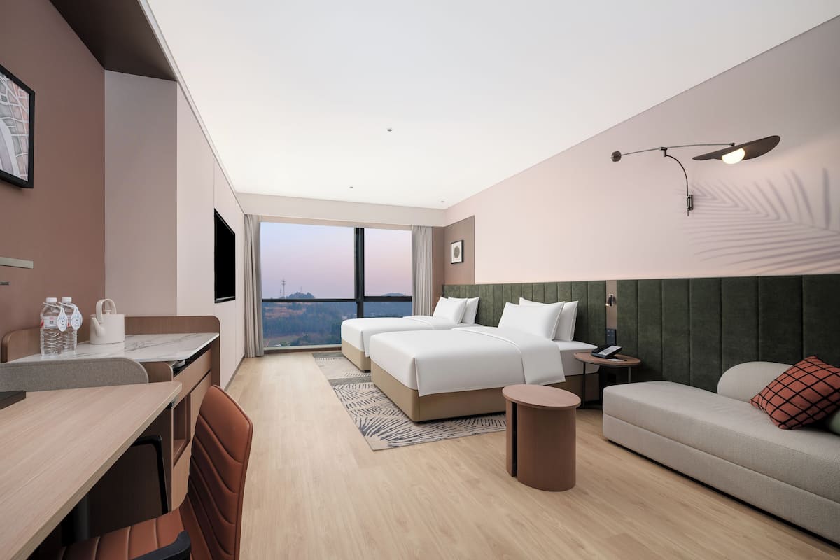 A modern hotel room with a bed, a sofa, a desk, and a view of the city.