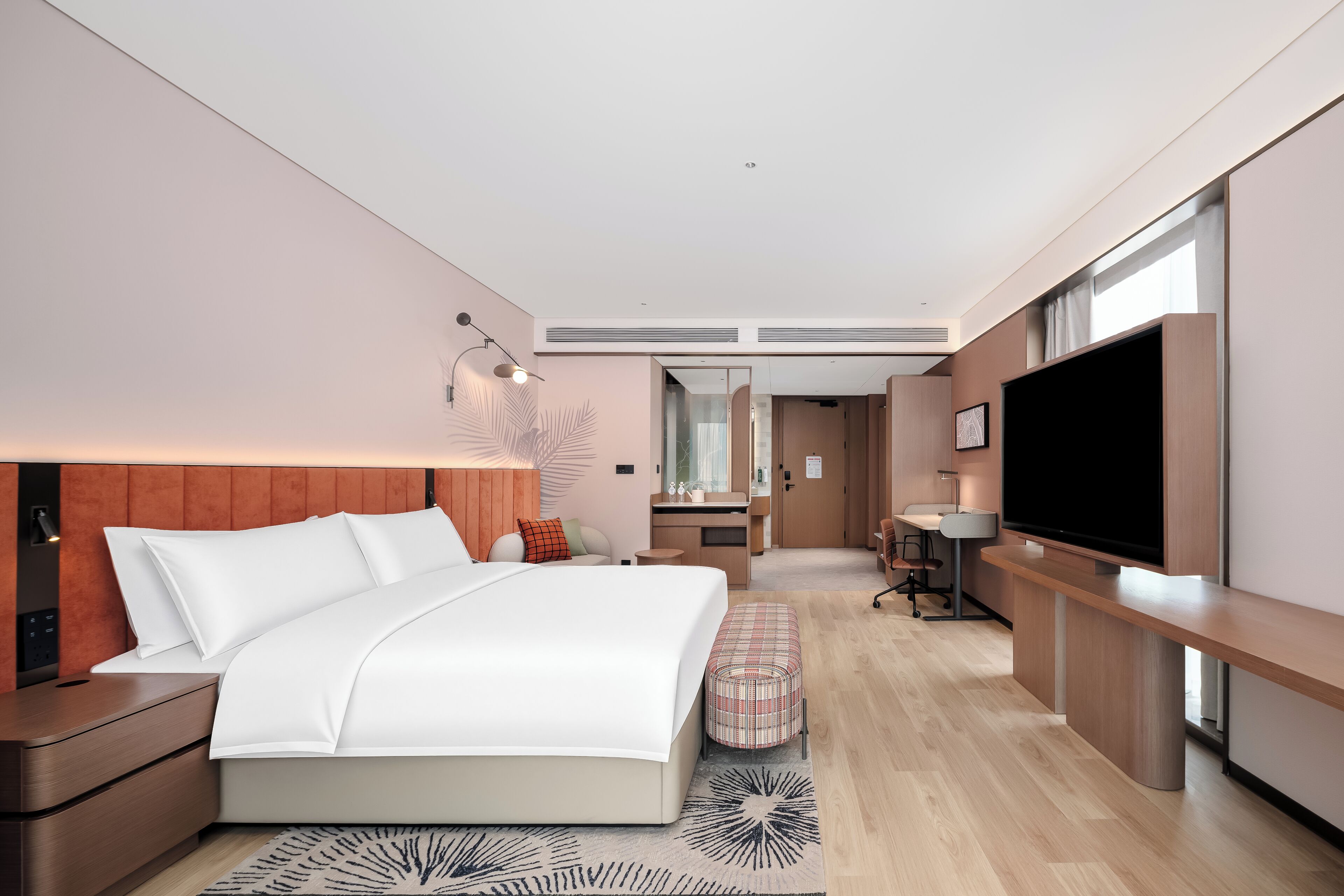 A modern hotel room with a bed, bedside table, TV, and a desk with a chair.
