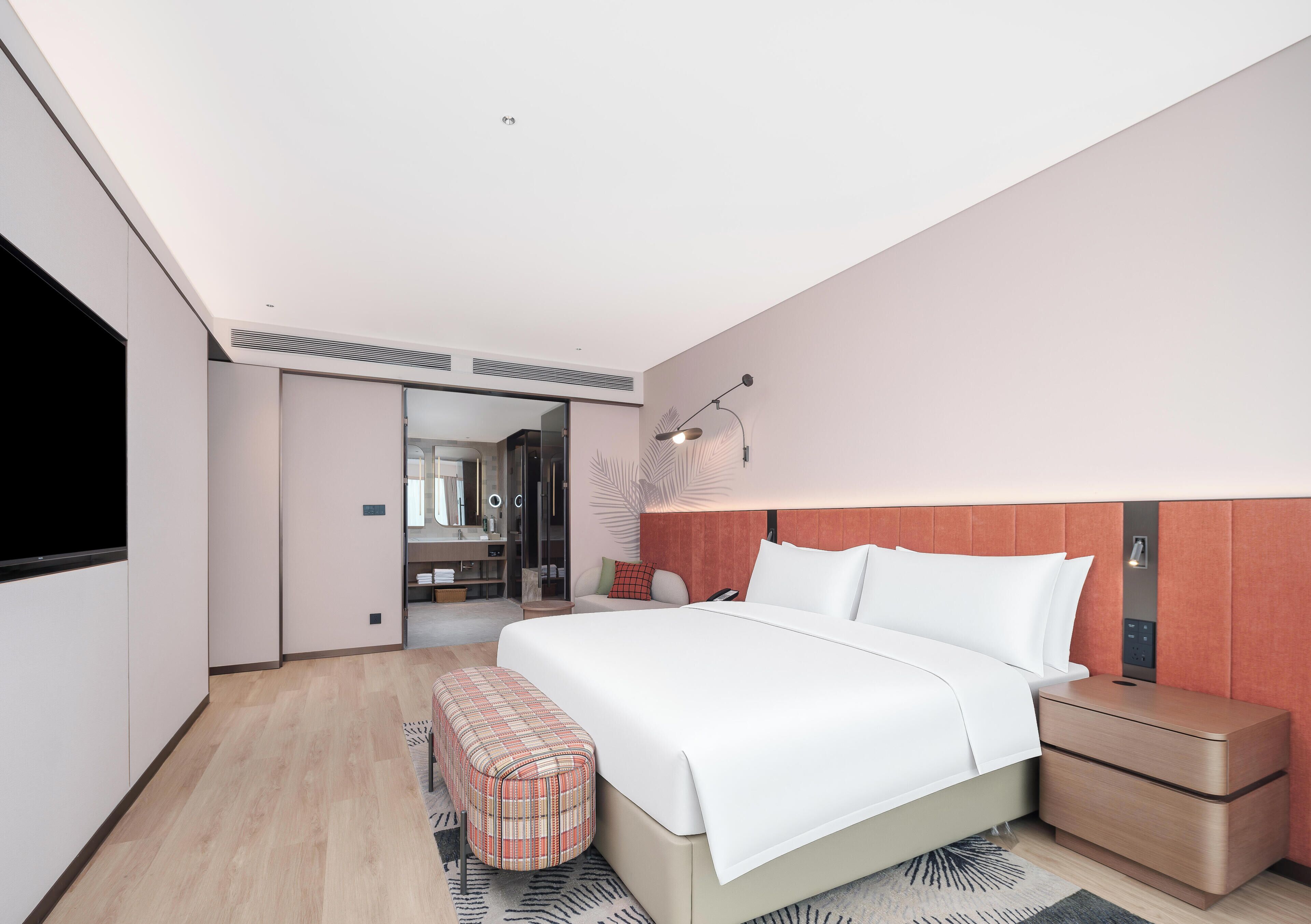 Una habitación de hotel moderna con una cama grande, mesitas de noche, un televisor de pantalla plana, un armario y un baño visible a través de una puerta abierta.