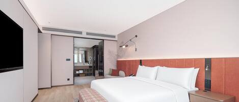 A modern hotel room with a large bed, bedside tables, a flat-screen TV, a wardrobe, and a bathroom visible through an open door.