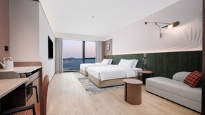 Une chambre d’hôtel moderne, dotée d’un grand lit, d’un canapé, d’un bureau et offrant une vue sur le paysage urbain.