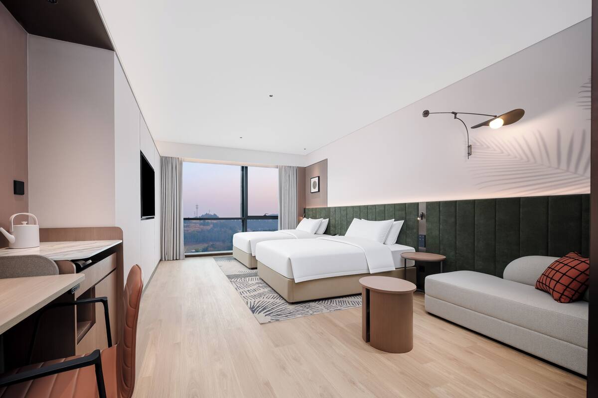 A modern hotel room with a large bed, a sofa, a desk, and a view of the cityscape.