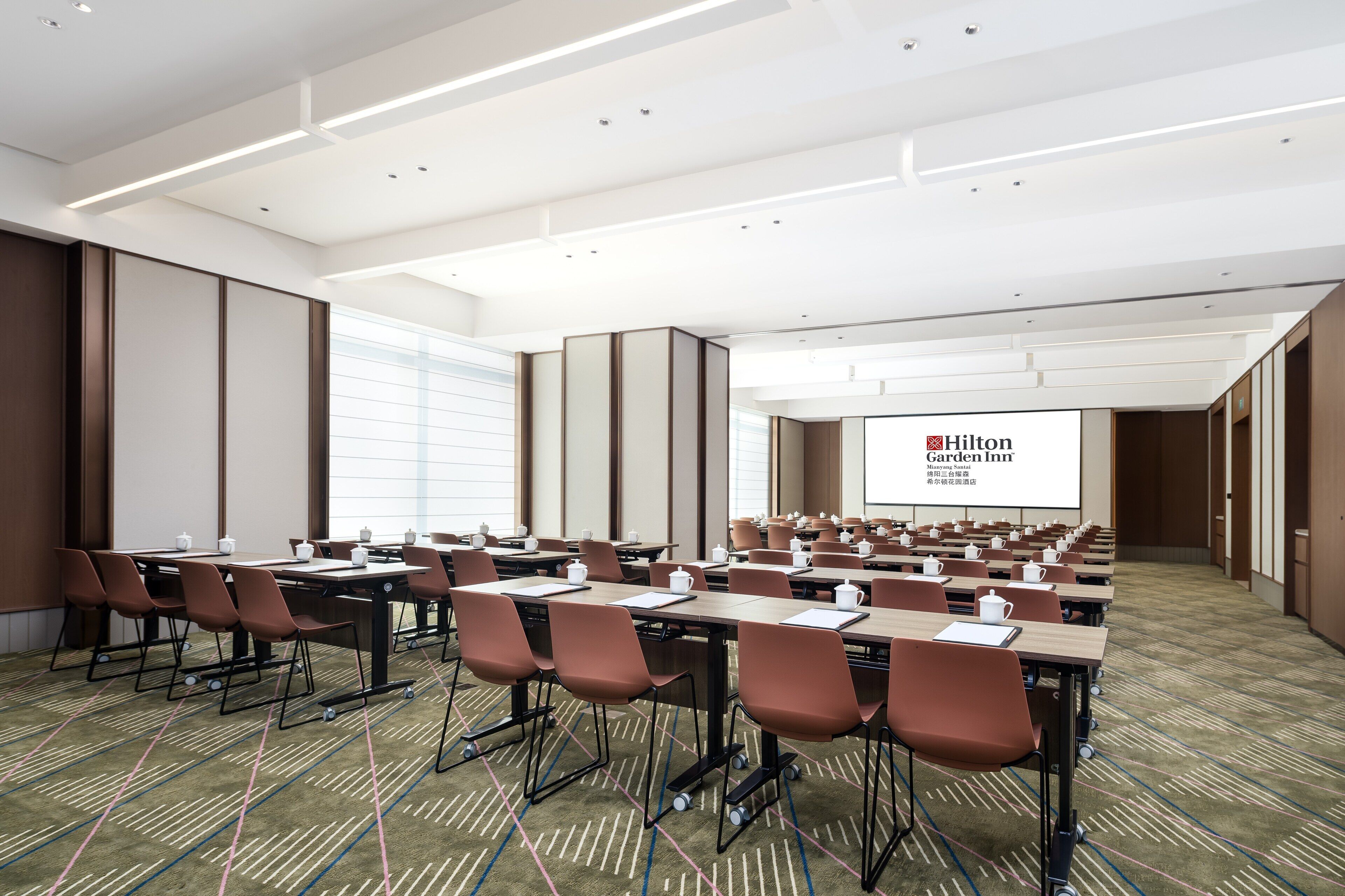 Une salle de conférence équipée de tables, de chaises et d’un écran de projection affichant le logo « Hilton Garden Inn ».