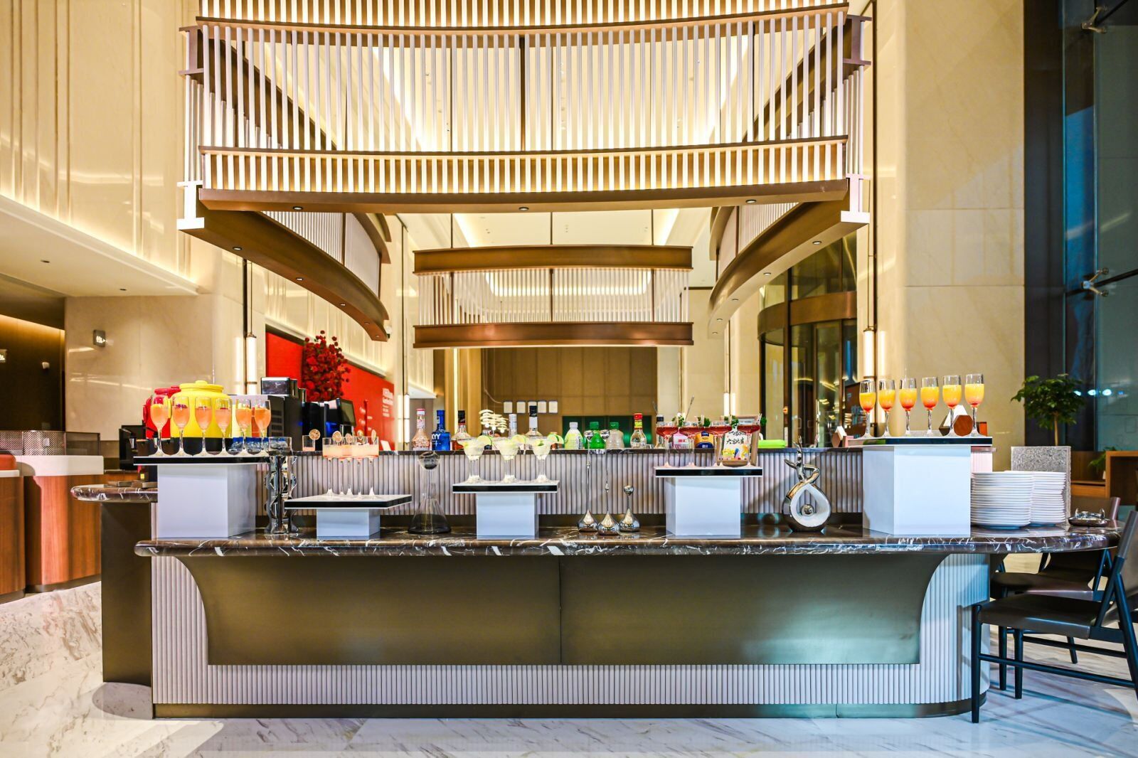 Un hall d’hôtel moderne doté d’un bar central, de différents espaces aménagés pour s’asseoir et offrant une vue sur l’intérieur.