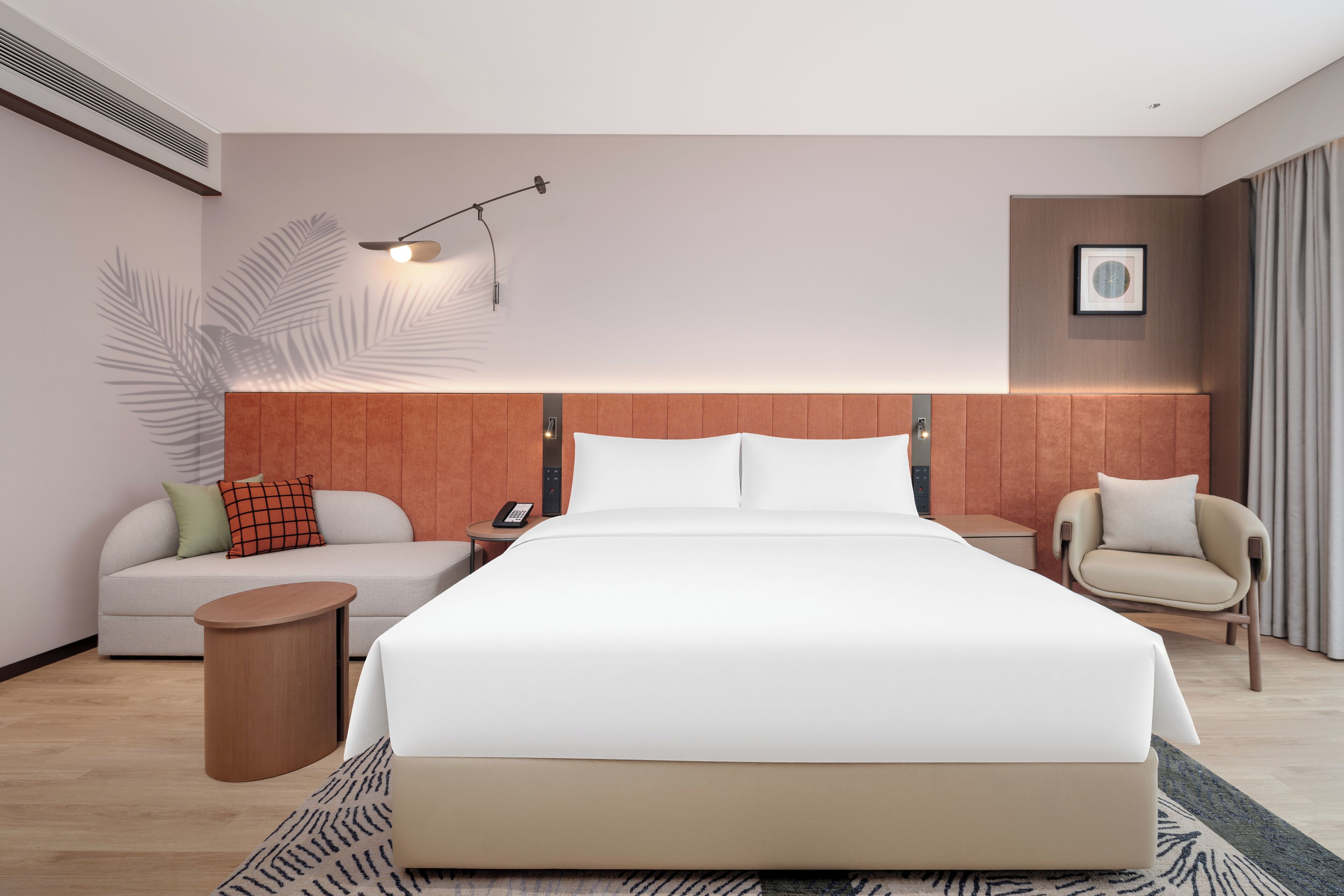 Una habitación de hotel moderna con una cama grande, un sofá, una silla, una mesita de noche, una lámpara y un cuadro en la pared.