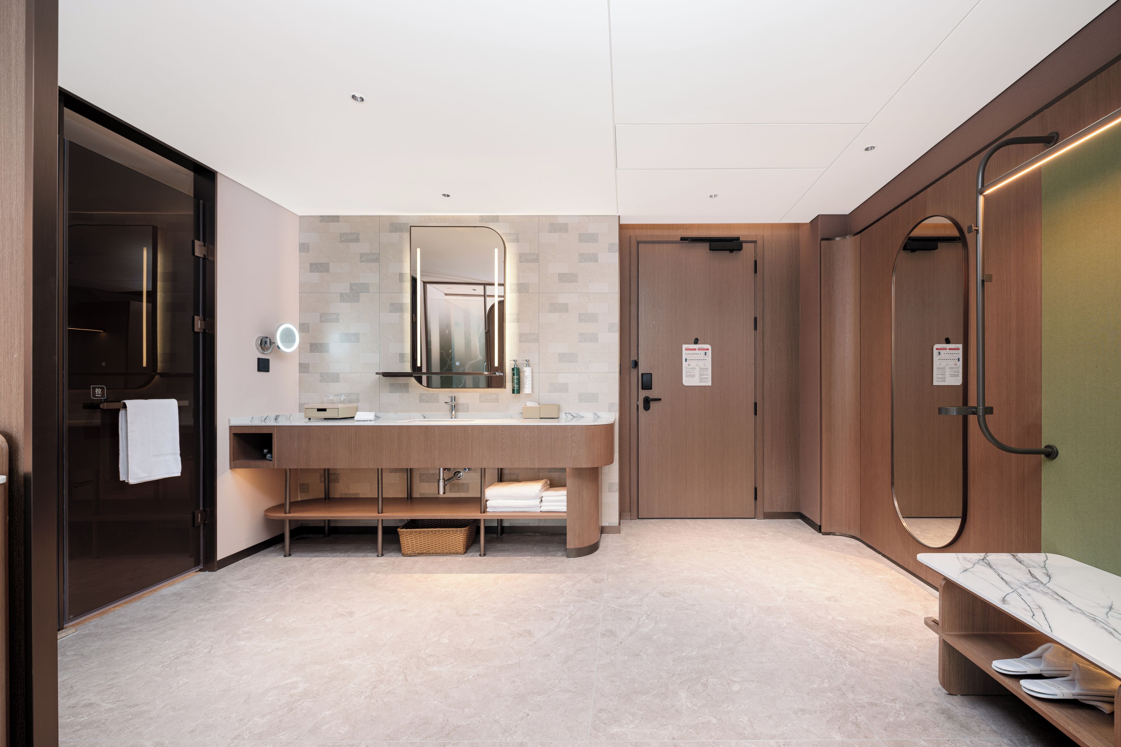A modern bathroom with a large mirror, a sink, a bench, and a shower area.