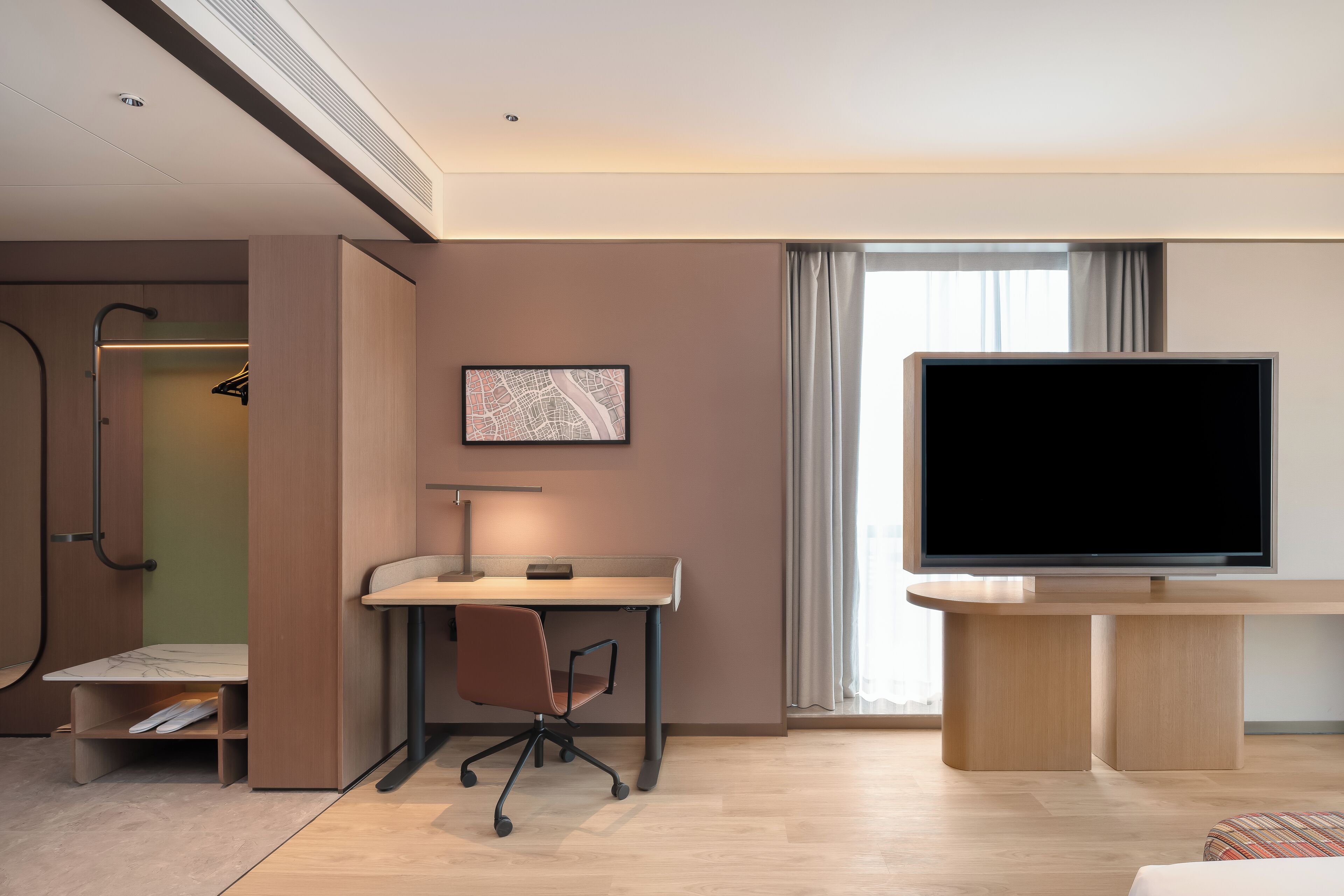 Ein modernes Hotelzimmer mit Schreibtisch, Stuhl, Fernseher und begehbarem Kleiderschrank.