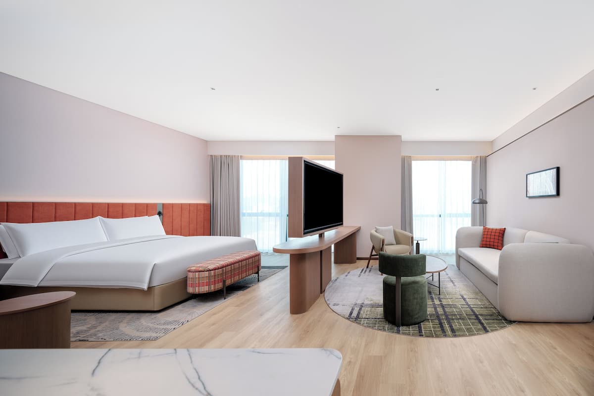 A modern hotel room with a bed, a flat-screen TV, a sofa, a small table, and a coffee table.