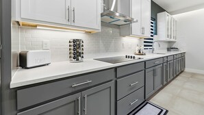 A modern kitchen with grey cabinets, a white countertop, a toaster, and a stove. - Palm Bay Luxury Haven (Palm Bay)