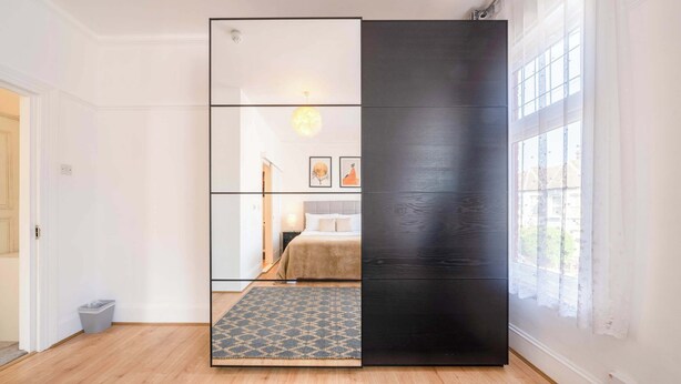 Una habitación con separador corredero, una cama con cabecera, un tapete estampado y un ventanal con cortinas.