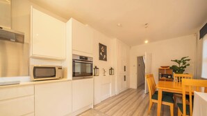 Una cocina moderna con armarios blancos, microondas, horno y comedor con mesa y sillas de madera.