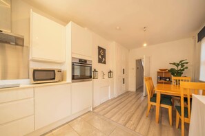 Eine moderne Küche mit weißen Schränken, einer Mikrowelle, einem Backofen und einem Essbereich mit einem Holztisch und Stühlen.