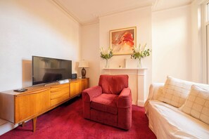 Ein Hotelzimmer mit einem Holzkapfen, einem roten Sessel, einem Bett mit weißer Bettwäsche, einem Flachbildfernseher, einer Blumenvase und einem Bild an der Wand.