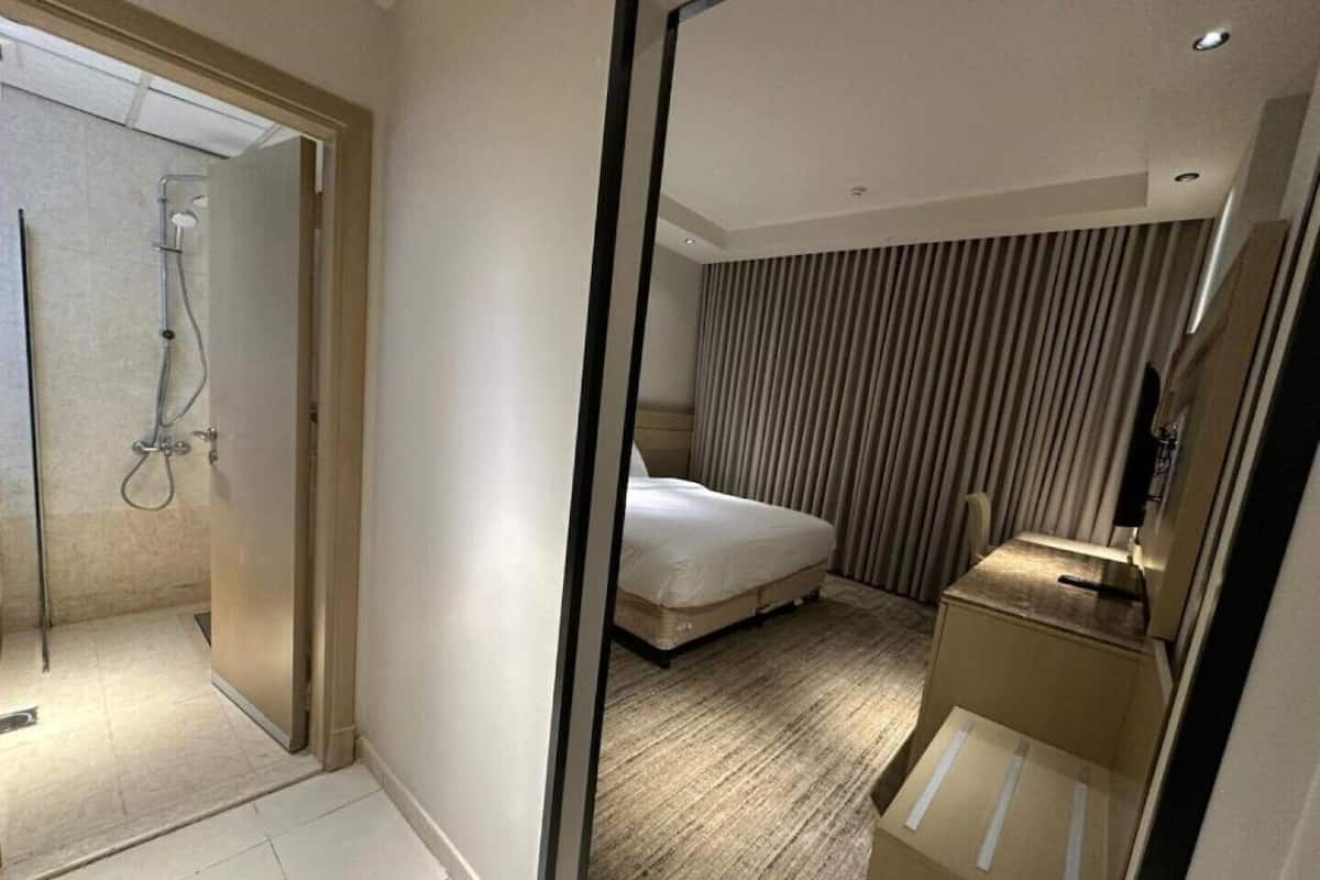 A hotel room with a shower, a bed, a bedside table, and a mirror.