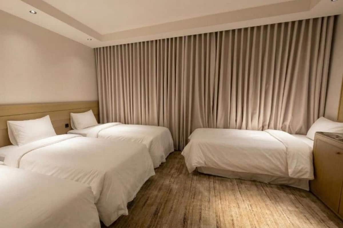 A hotel room with two single beds, a wooden headboard, a large window with curtains, and a wooden floor.