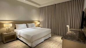 A hotel room with a bed, two bedside lamps, a nightstand, a wooden floor, a large window with curtains, and a flat-screen TV mounted on the wall. - Manazel Alzaereen Hotel 2 (Makkah)