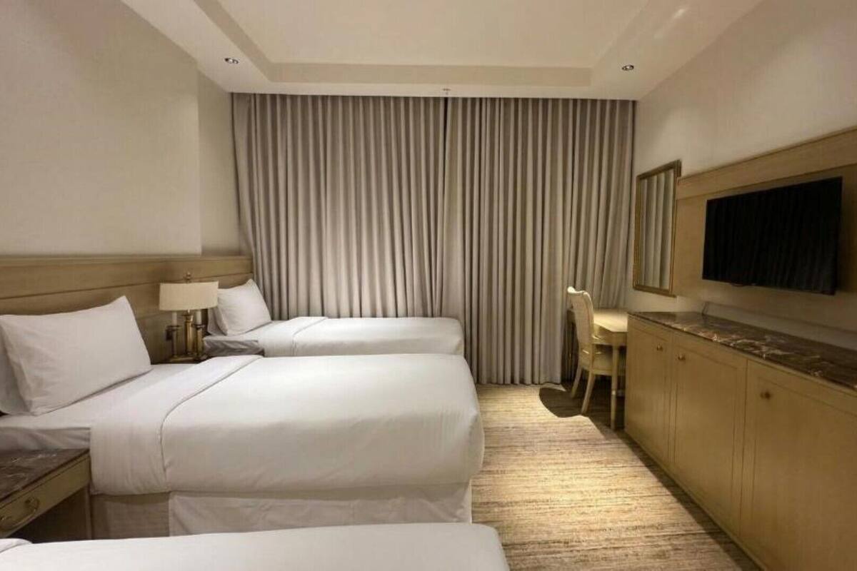 A hotel room with two beds, a desk, a chair, a TV, and a large window with curtains.