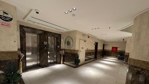 A hotel lobby with a reception desk, a glass elevator, and a marble floor. - Manazel Alzaereen Hotel 2 (Makkah)
