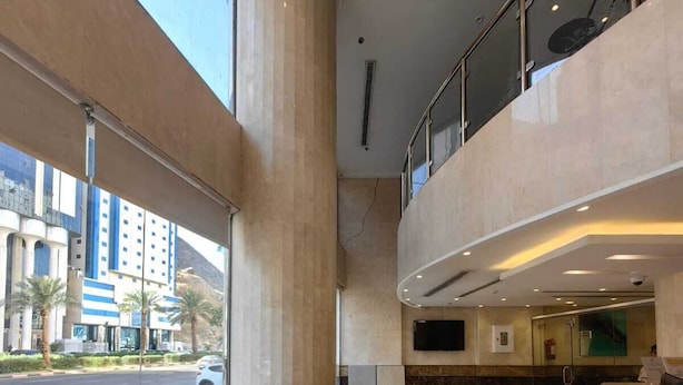A spacious lobby with a high ceiling, a large window offering a view of the city, and a modern reception area. - Manazel Alzaereen Hotel 2 (Makkah)