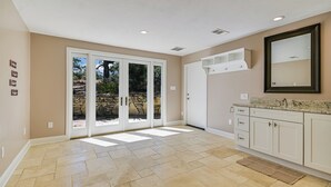 Un baño espacioso con una zona de ducha amplia, tocador con espejo y pared de piedra visible a través de las puertas de cristal.