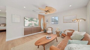 A spacious living room with a large TV, comfortable seating, a ceiling fan, and a view of the outdoors. - Luxury Villa 3 Blocks to Beach, Saltwater Pool, Outdoor Oasis, firepit, sunlounge's, mini putt and close to all the area has to offer. (Cape Canaveral)