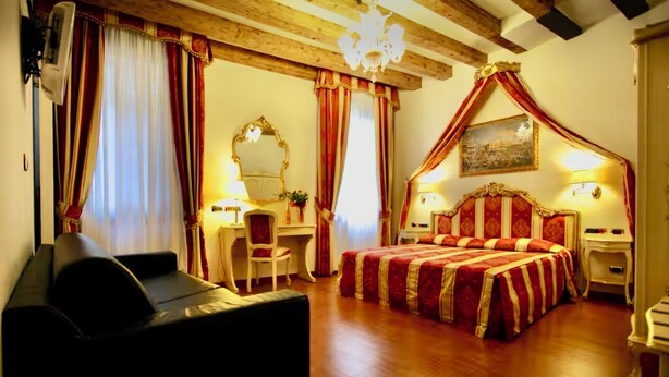 Habitación de hotel con una cama grande, un escritorio, una silla, un sofá, un espejo y una araña.