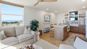 Uma sala de estar moderna com um sofá bege, área de jantar e cozinha com ilha central.