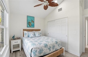 A bedroom with a bed, a nightstand, a ceiling fan, a door, and a wall painting. - Clear Day - Luxury on the Water (Fort Myers Beach)