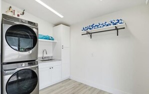 A laundry room with stacked washers and dryers, a sink, and a shelf with folded towels. - Clear Day - Luxury on the Water (Fort Myers Beach)
