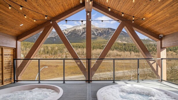 A hot tub area with a wooden deck and a view of mountains. - Brand New 1BR Canmore Retreat: Hot Tub, Sauna, Gym (Canmore)