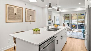 A modern kitchen with a central island, pendant lighting, and a view to the outdoors. - Brand New 1BR Canmore Retreat: Hot Tub, Sauna, Gym (Canmore)
