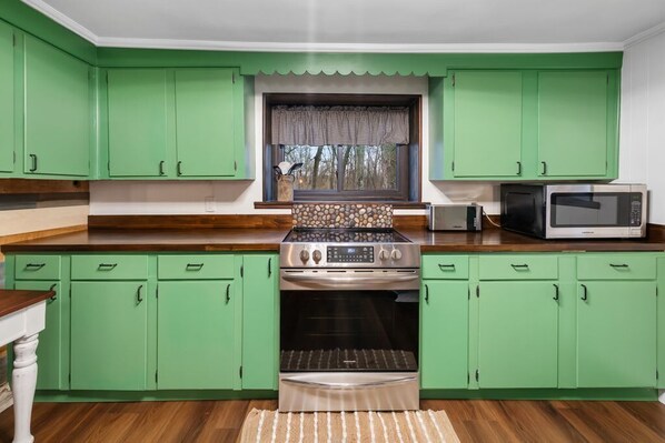 Une cuisine avec des meubles de couleur verte, une cuisinière, un four et un four à micro-ondes.