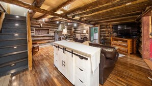 L’intérieur d’une cabane en rondins est doté d’un escalier en bois, d’un espace salon central avec un canapé et une table basse, ainsi que d’un téléviseur posé sur un meuble en bois.