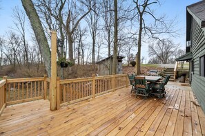 A wooden deck with a table and chairs, surrounded by trees and a small shed. - Pearl’s Place- a Creekside Cabin (Union Township)