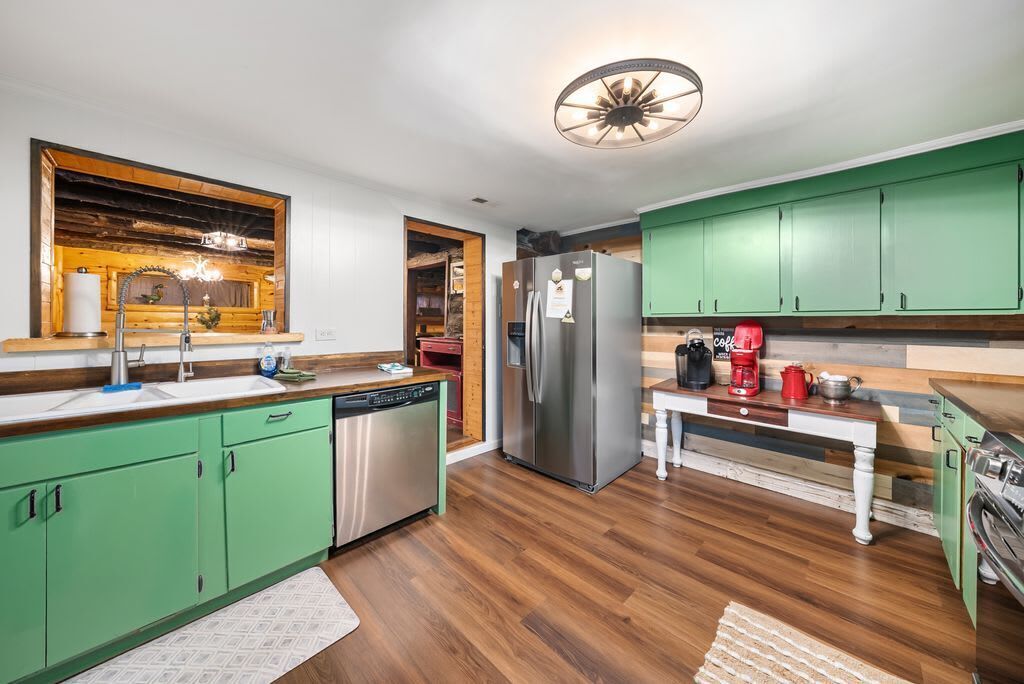 A modern kitchen with green cabinets, stainless steel appliances, and a wooden floor.