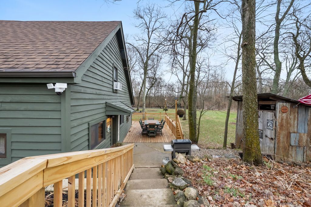 A wooden deck leading to a house with a green exterior and a covered outdoor seating area.