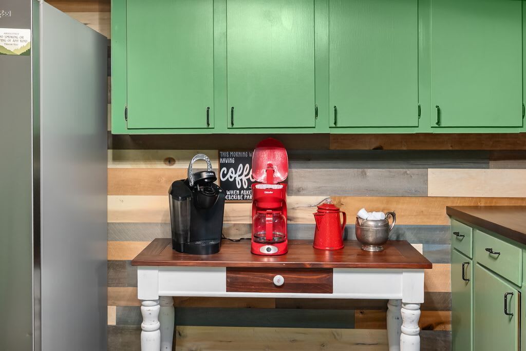 A kitchen with green cabinets, a wooden countertop, a coffee maker, a kettle, and a mug.