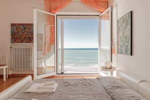 Ein Schlafzimmer mit Bett, Meerblick und einem Vorhang vor dem Fenster.