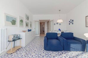 Ein modernes Wohnzimmer mit einem blauen Sofa, einem Essbereich mit Tisch und Stühlen sowie einer Küche im Hintergrund.