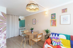 Una sala moderna con una mesa redonda de madera, dos sillas, un sofá colorido y una lámpara de techo.