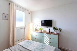 A bedroom with a bed, a dresser with drawers, a television mounted on the wall, and a window with curtains. - LA TERRAZZA SUL MARE - Sanremo (Sanremo)